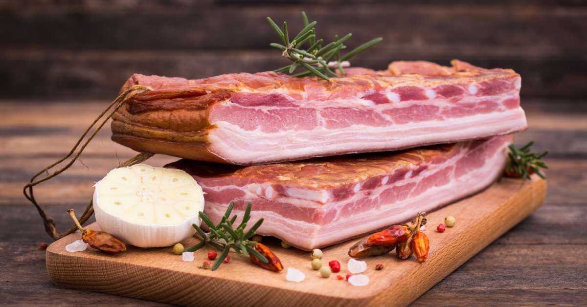 Crispy, smoked bacon served on a wooden board. Various garnishes top the dish, adding color to the plate.